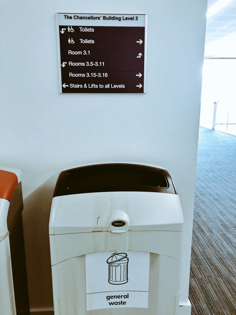 Visual and tactile signage in university building - placed on wall over the top of large, smelly bin