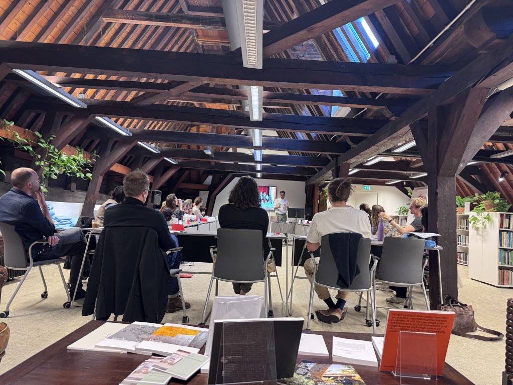 Abhay talking to academic researchers in an Amsterdam room at the top of old building so full of thick wooden roof planks