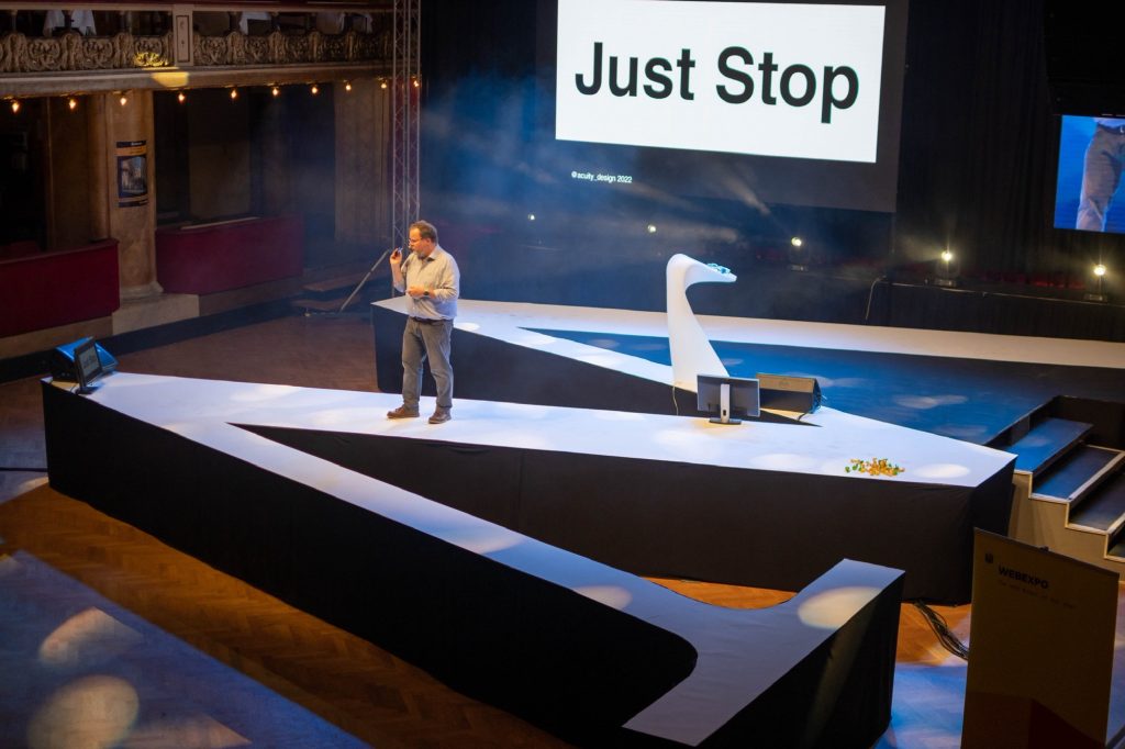 Alastair on stage shaped like a W with slide saying Just Stop in background