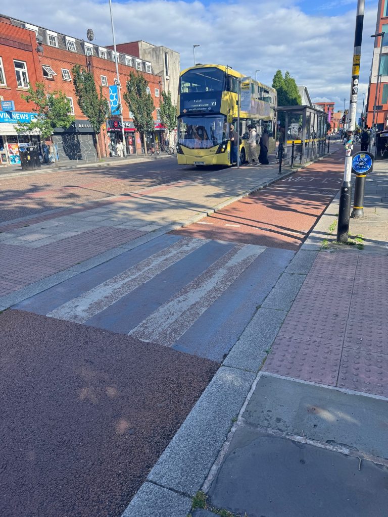 Black and white paint on croassing is very worn away and underlying red tarmac colour shows through.